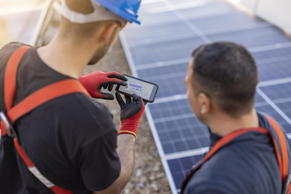 two workers reviewing their solar panel installation on a smart phone
