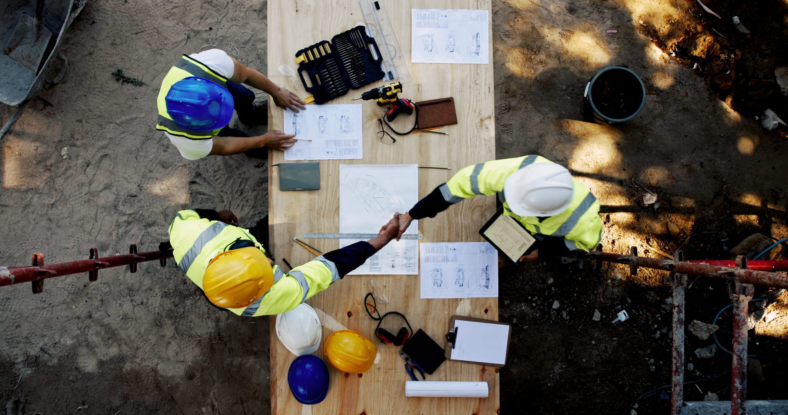 Two commercial contractors shaking hands over blueprints after a successful commercial building inspection to avoid sunk costs.