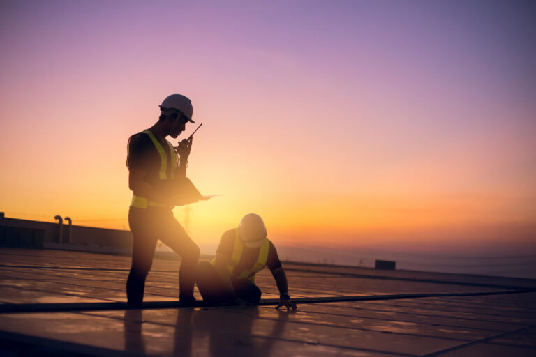 Two solar panel installers in hard hats and high-visibility vests working on a rooftop solar array at sunset in Texas