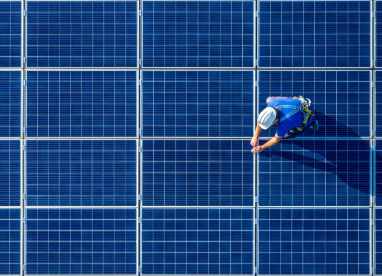 Solar panel technician in safety harness inspecting photovoltaic panels on a rooftop solar installation.