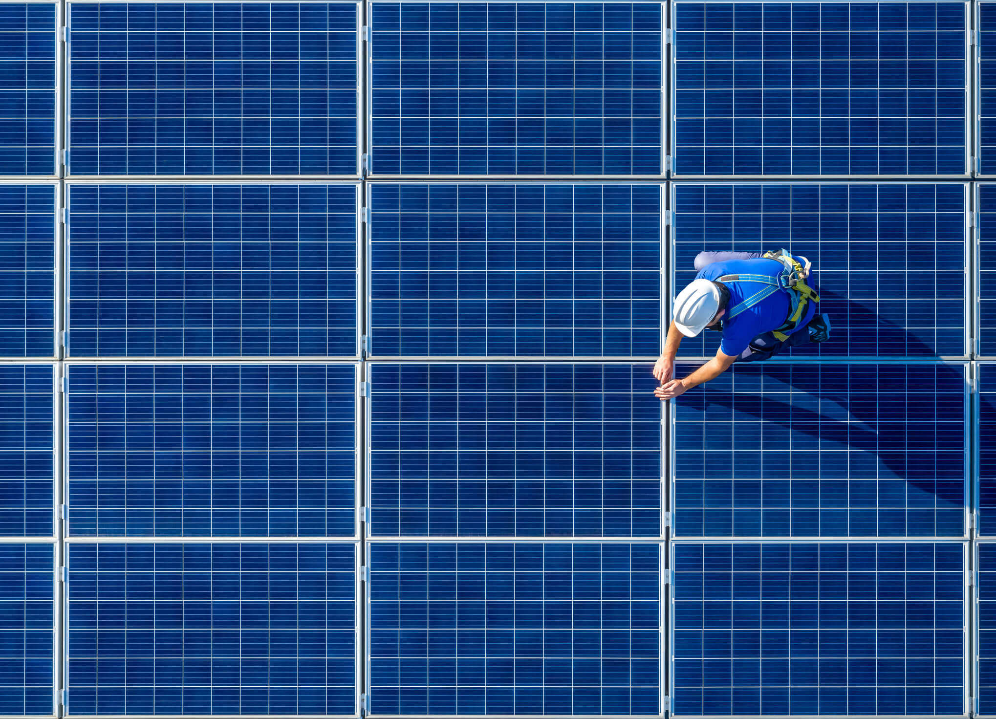 Solar panel technician in safety harness inspecting photovoltaic panels on a rooftop solar installation.