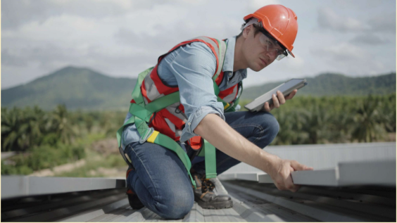 Roofing contractor in a safety harness conducting a fall roof inspection on a metal roof